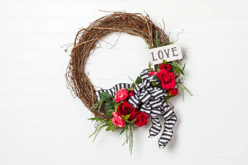 DIY Valentines Wreath with red roses, black and white ribbon bow and hand painted sign hanging on the wall 