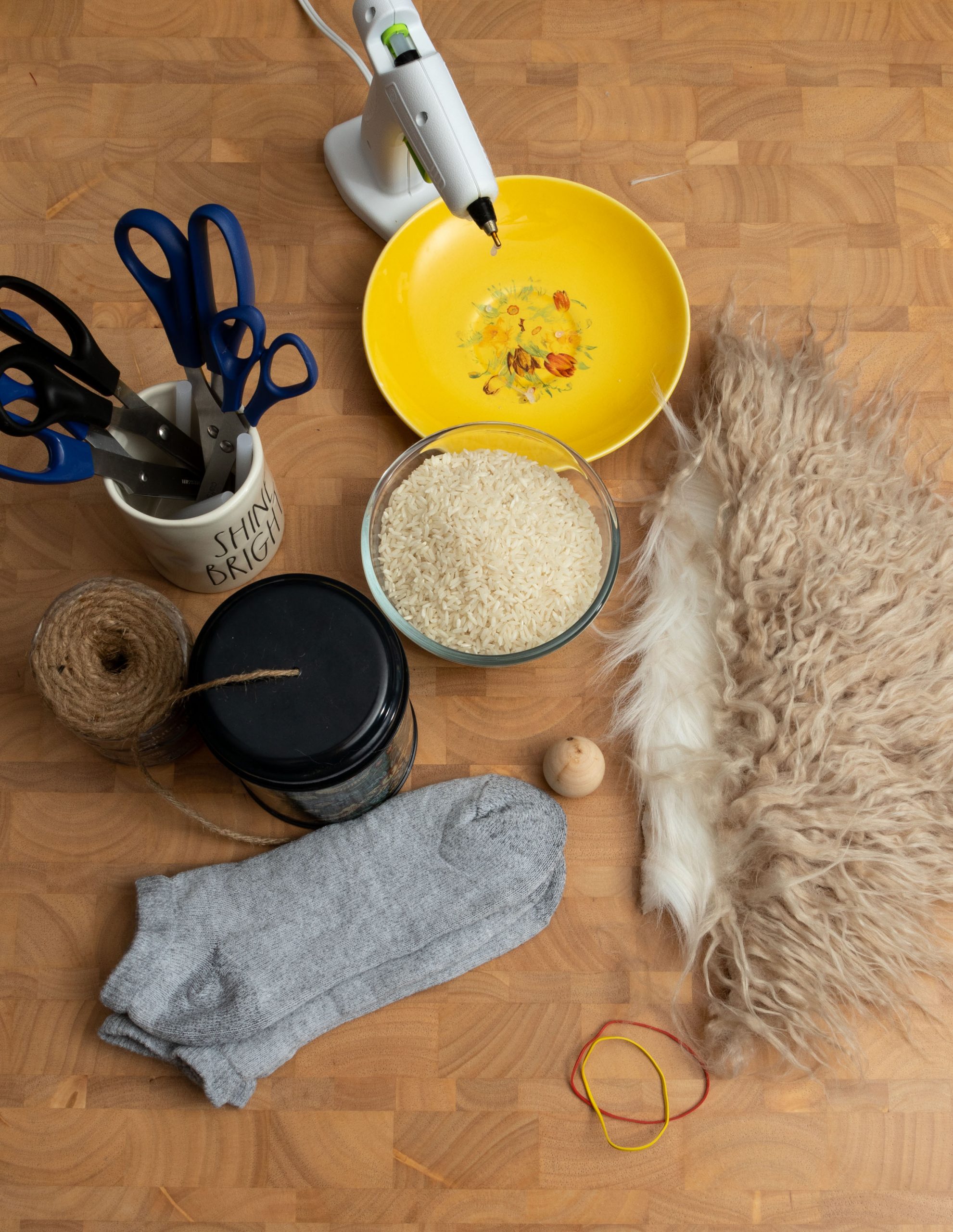 Gnome supplies: hot glue, scissors, rubber band, rice, faux fur, wooden bead, socks, and twine sitting on the table. 