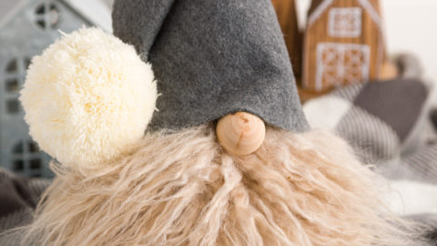 DIY Gnome with a faux fur beard and gray felt hat. Sitting on a gray and while buffalo check throw blanket.