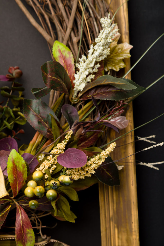 Closeup view of the floral on the grapevine wreath show the muted fall colors. Purples, golds, and greens are beautiful in your Handmade fall wreath. Learn how to make one today. Closeup view of the floral on the grapevine wreath