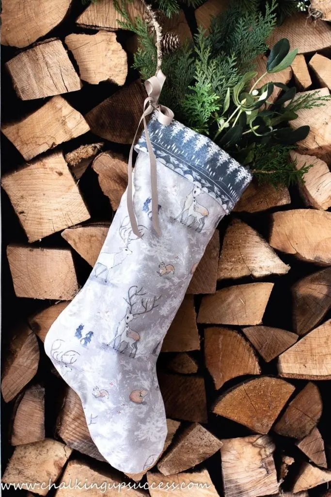 Tan and blue handmade stocking filled with greenery hanging from a stack of chopped wood 