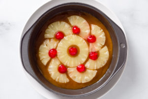 Pineapple slices and cherries arrange in a pan over the butter and brown sugar mixture