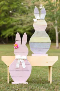 DIY Wooden Bunnies that have been painted for Easter standing the yard with bows