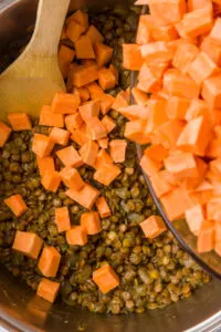 Adding diced sweet potatoes to lentils and onions
