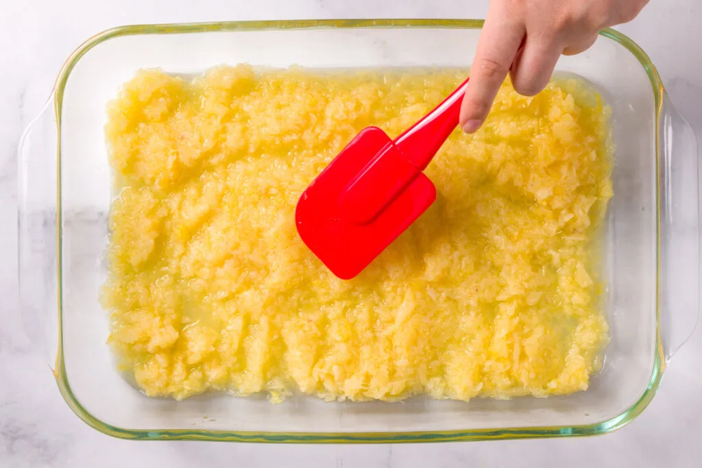 Using a spatula to evenly spread the crushed pineapple