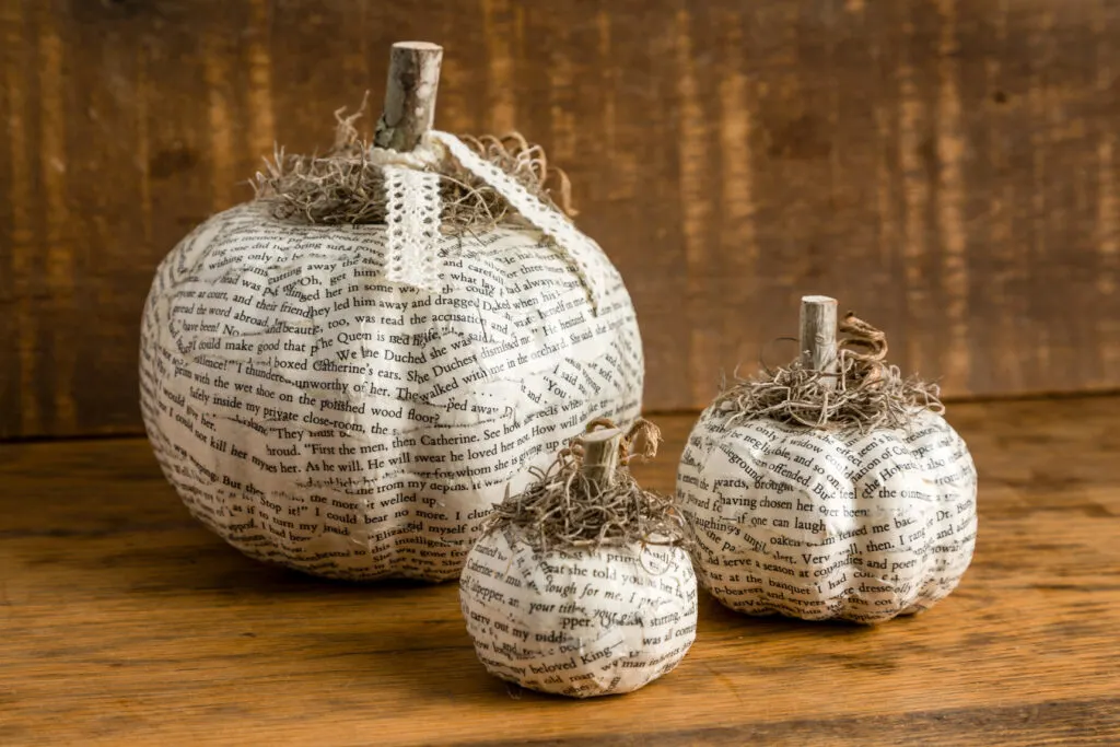 Three Book Page Decoupage Pumpkins sitting on a wood table 