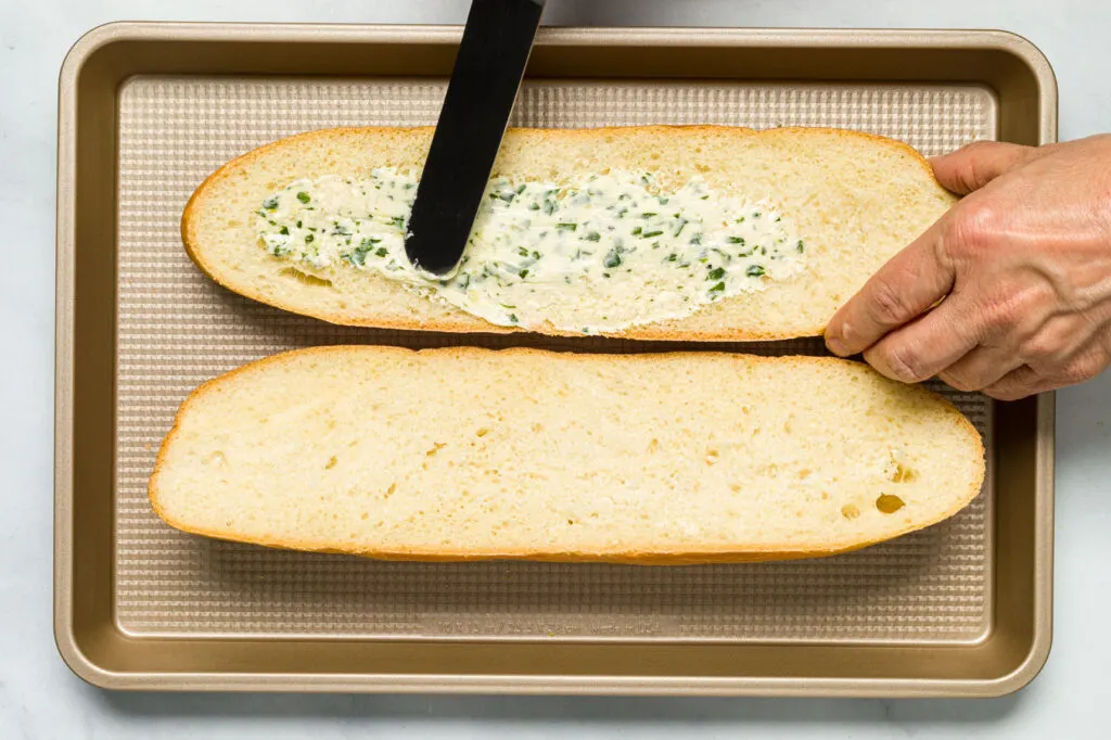 Spreading some garlic and herb butter on the cut sides of the bread 