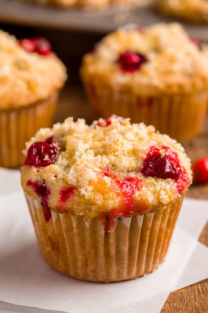 Cranberry orange muffins with orange zest sugar topping sitting on a wood tabel