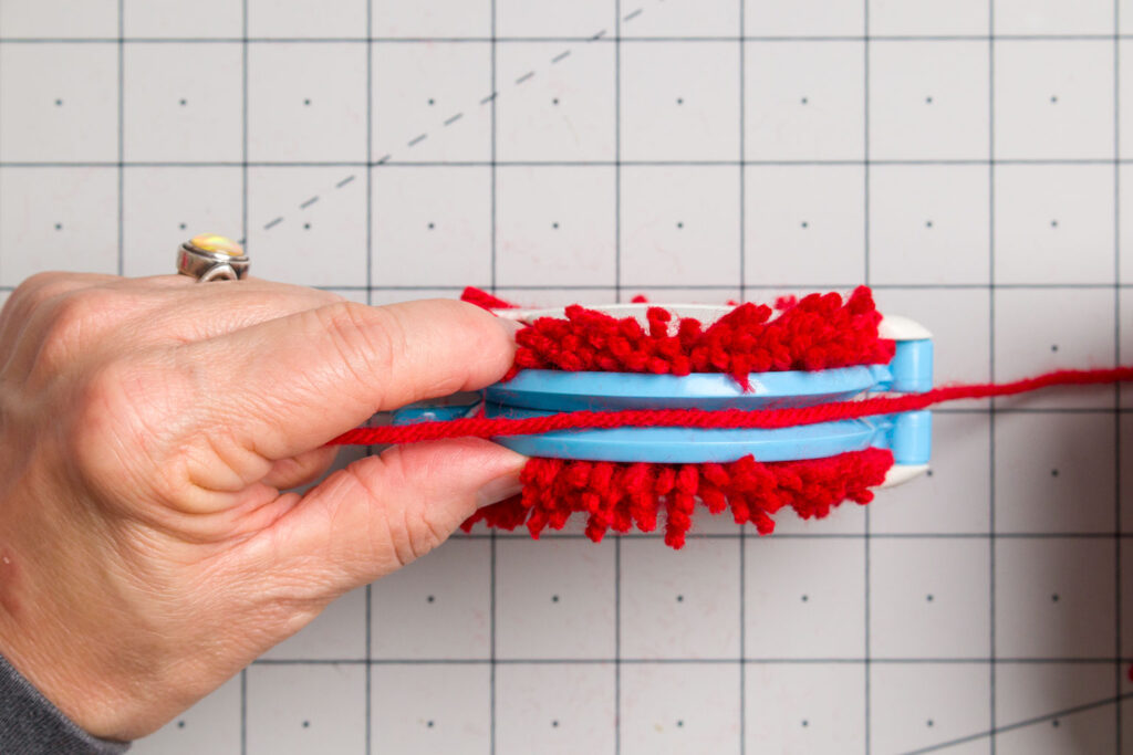 Wrap a yarn time around the center of the pompom maker 