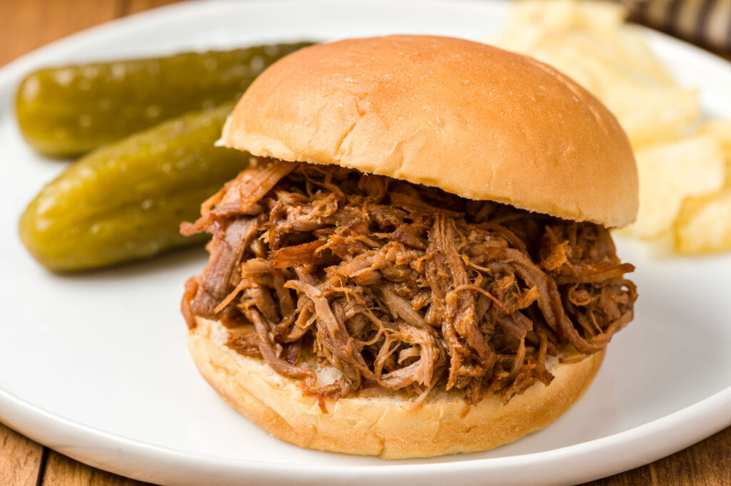 Pulled pork Sandwich on a plate with pickles and potato chips