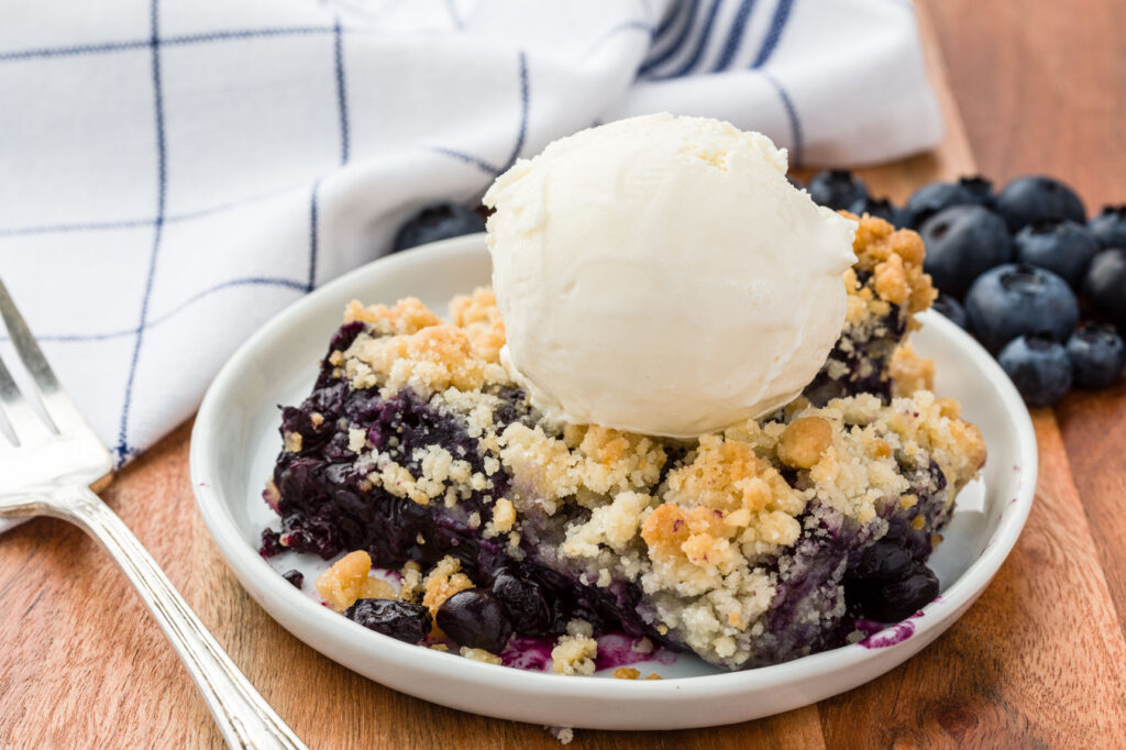Blueberry crisp topped with vanilla ice cream on a small plate