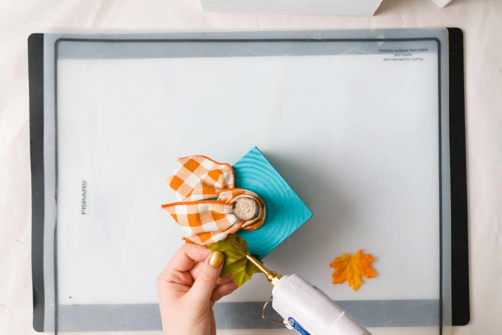 Gluing purchased leaves on the turquoise pumpkin