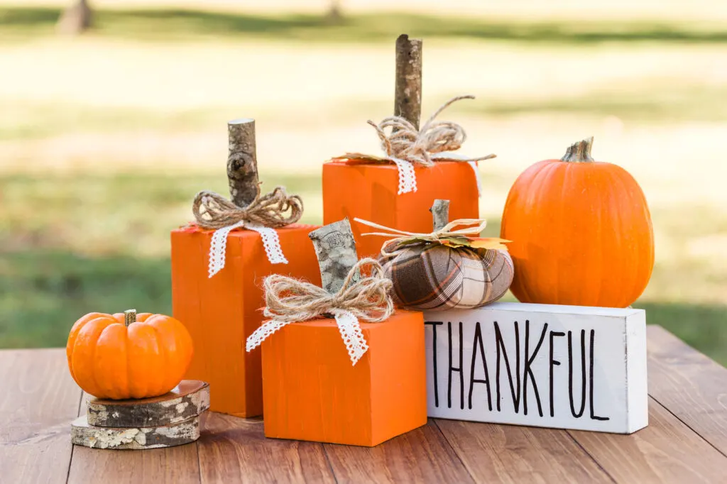 Wood pumpkins painted orange with a handmade sign and pumpkins on a wood table