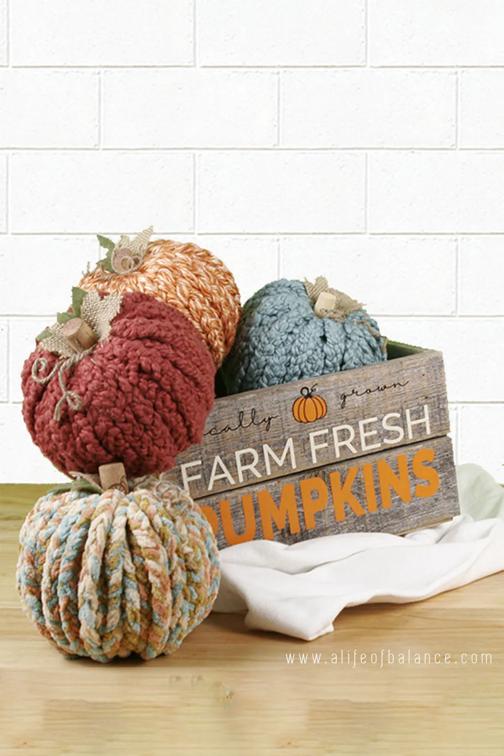 Braided yarn covered pumpkins in wooden box sitting on a table