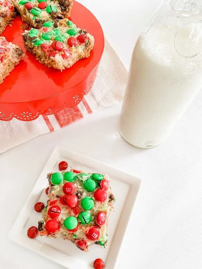 Christmas Magic Cookie Bars with red and green m and m's served with a glass of milk