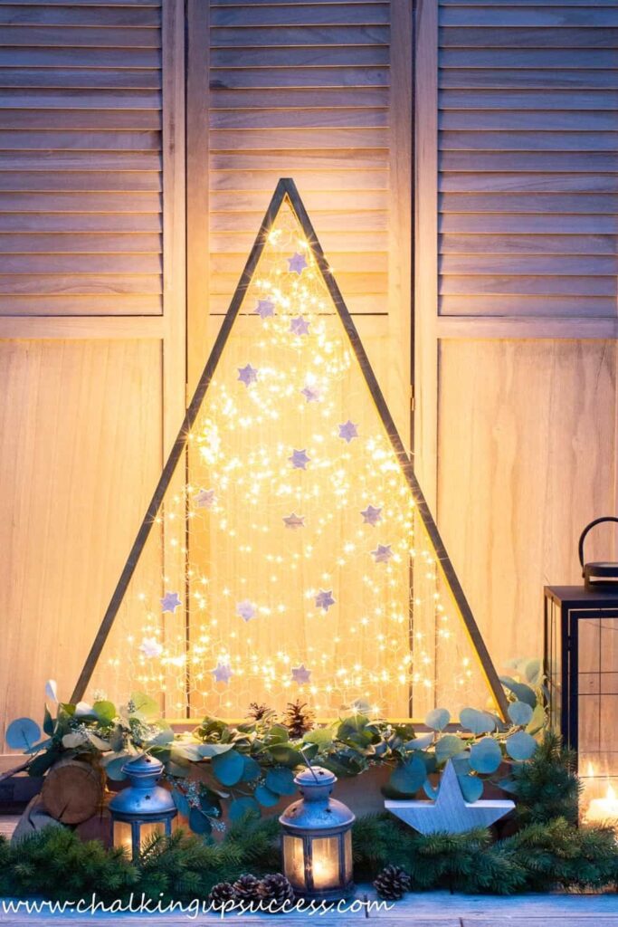 DIY Wooden Triangle Christmas Tree with Christmas lights sitting on a tqble