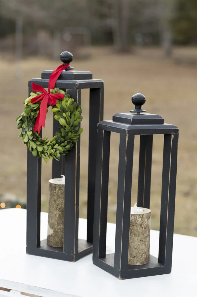 DIY Wooden Lanterns with tea lights and a small wreath and red bow outside on a bench