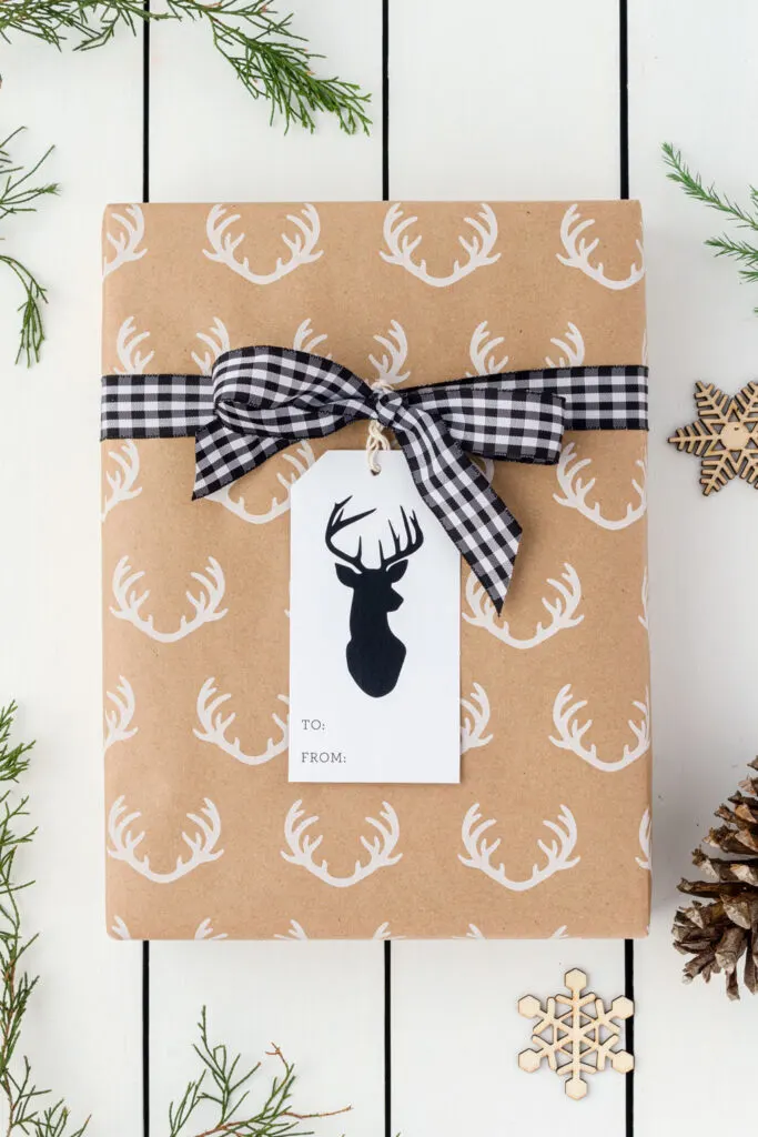 Tan gift wrap with white deer heads with a black and white checked ribbon bow and a deer tag