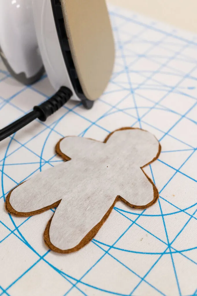 Felt Gingerbread man with the fusible interfacing place on the backside of the felt cutout sitting in the pressing mat with the iron