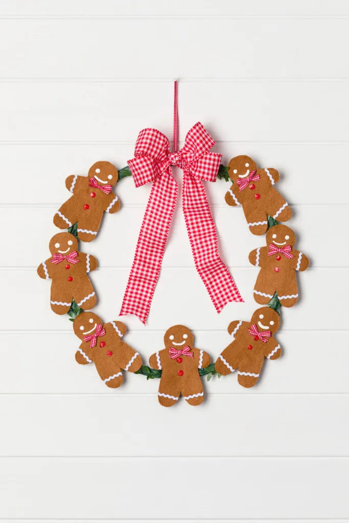 DIY Gingerbread Wreath with red and white check bow hung on a wall