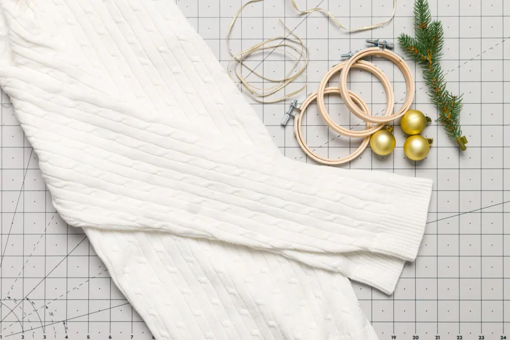 supplies to make sweater ornaments (sweater, Christmas bulbs, greenery, embroidery hoops, and ribbon)