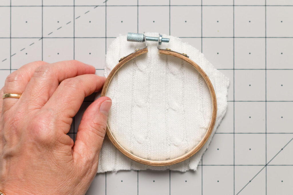 Placing the stained outer ring of the embroidery hoop with the piece of sweater on a cutting mat