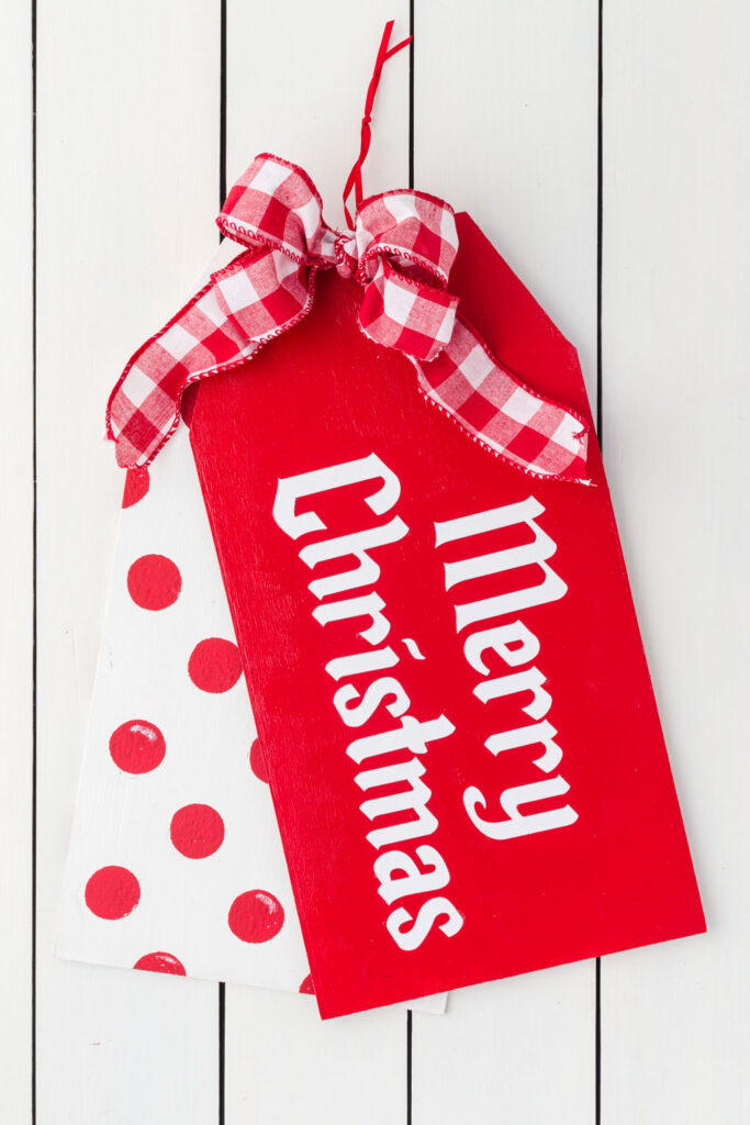 Merry Christmas door hanger with red and white check bow sitting on a wood table
