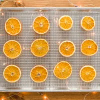 Dried Orange Slices on a wire rack in a sheet pan sitting on a wood table with fairy lights and snowflake oraments