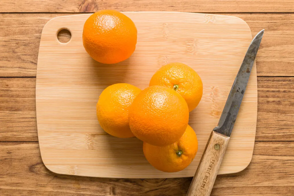Florida oranges on a bamboo cutting board with a knife on a wood table