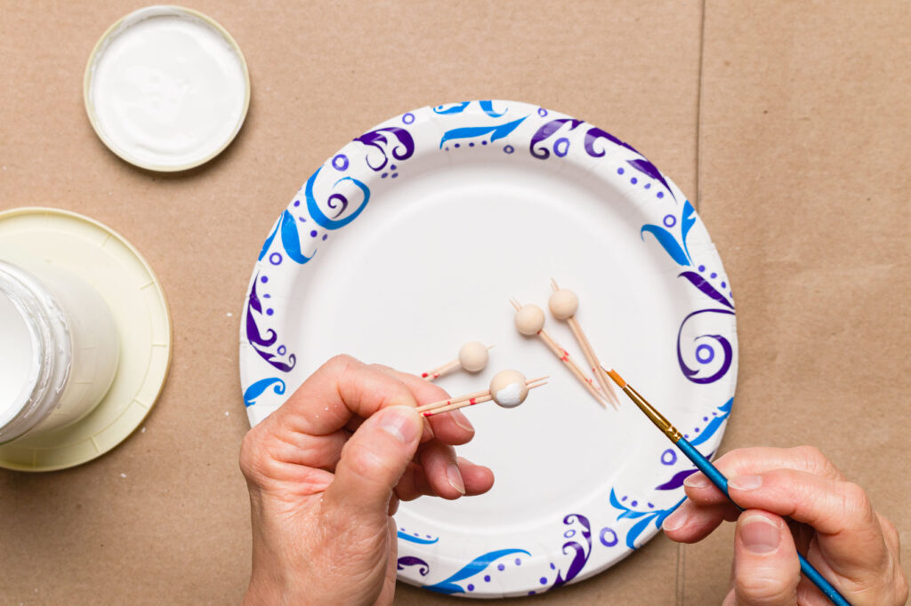 Painting the wood beads on toothpicks with white paint