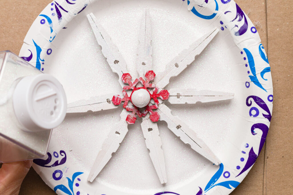 Adding glitter to White painted snowflake with a red accent and white bead center
