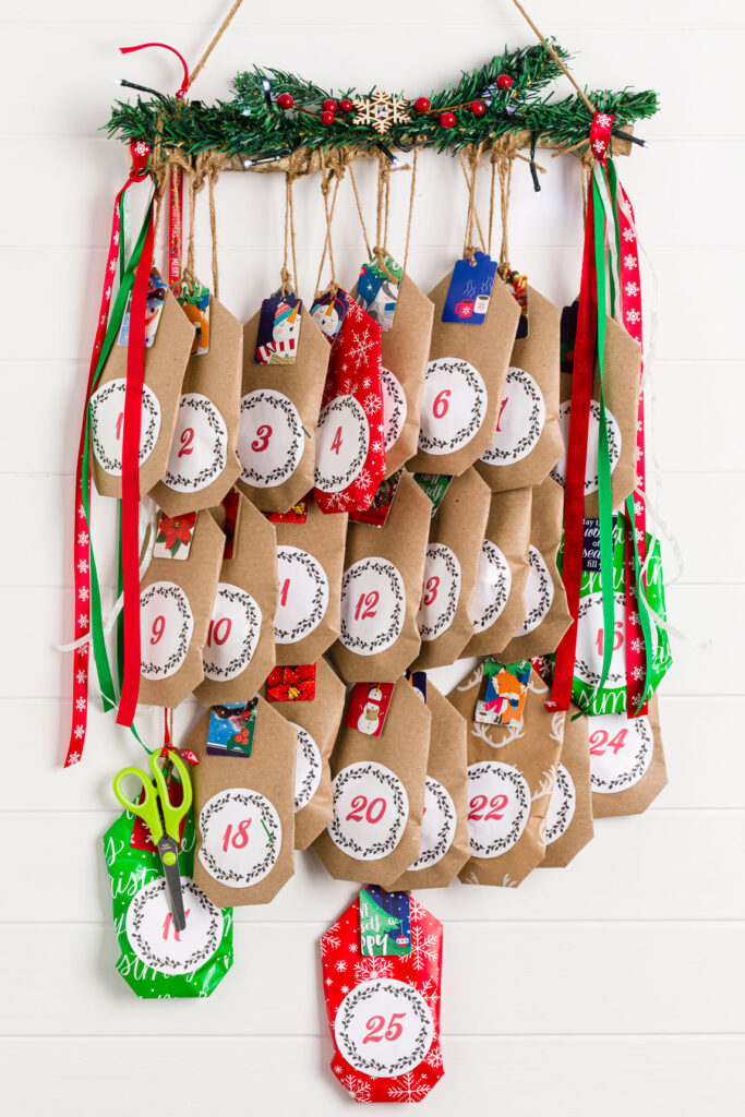 Christmas Candy Calendar hanging on wall with greenery, red berries and fairy lights