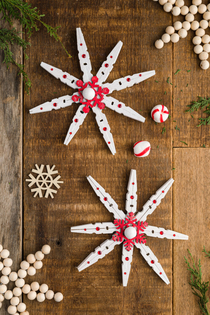 Two painted clothespin snowflakes with wood bead ornaments on a wood table