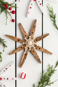 Clothespin Snowflakes DIY Clothespin snowflakes with peppermint candies, cedar branches and berries on a wood table
