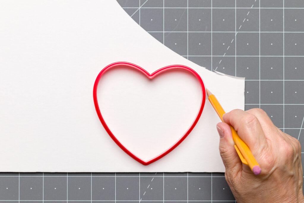 Using a pencil to trace around my heart-shaped cookie cutter on foam core on a cutting mat
