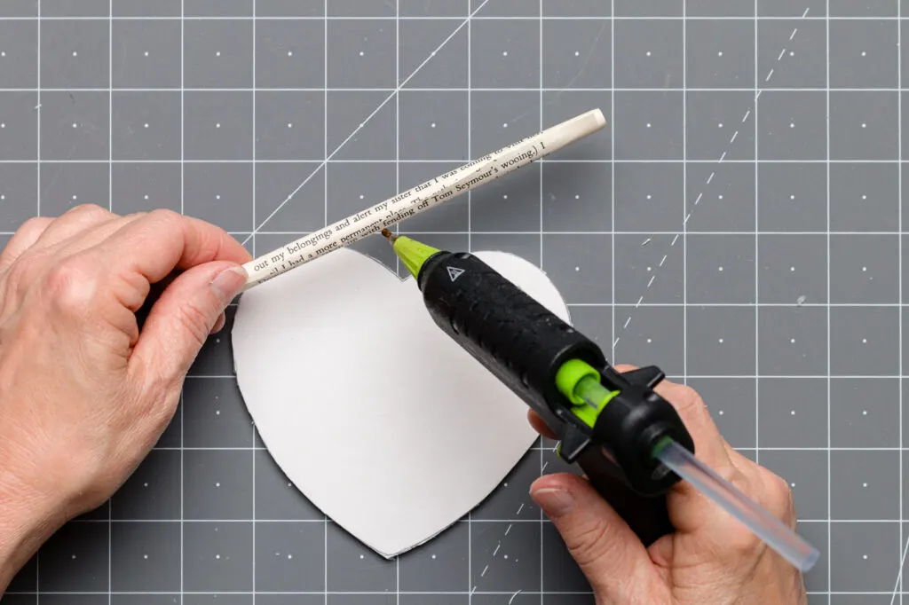 Applying hot glue along the seam of the paper roll on a craft mat