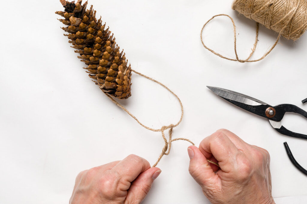 Knotting the hanger string that is attached to pine cone 