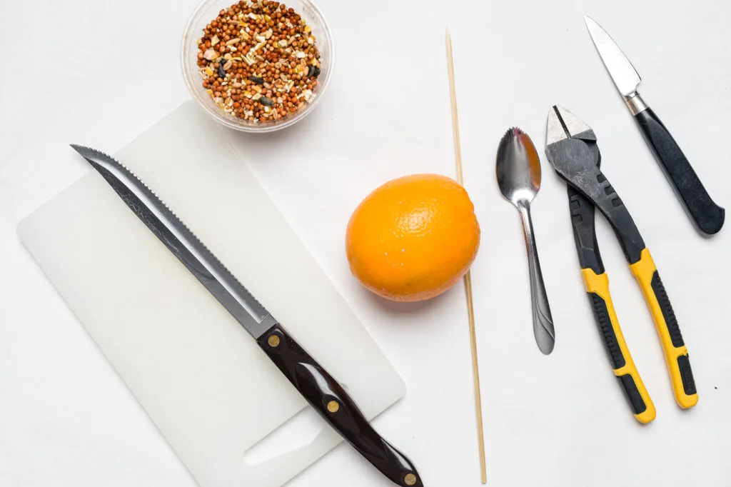Supplies for creating orange bird feeders. Orange, knife, cutting board, grapefruit spoon sitting on a table