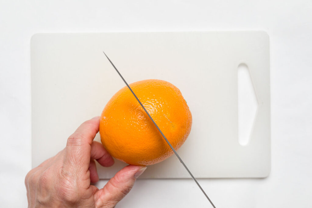 Cutting an orange in half on a cutting board with a knife