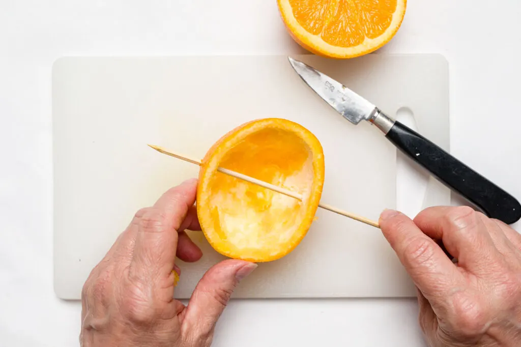 Pushing a wooden skewer through the orange peel half