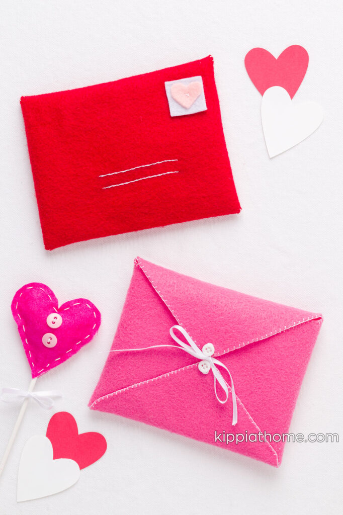 A red and pink felt envelope pm a table with paper hears and a fabric heart