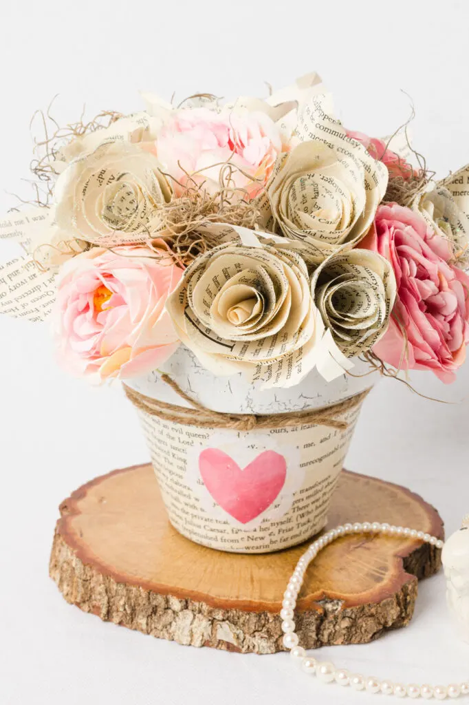 Silk and paper rose flower arrangement in a painted flower pot on a wood slice