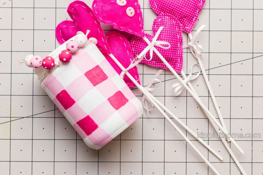 fabric hearts attached to skewers and a hand painted buffalo check jar on a craft mat