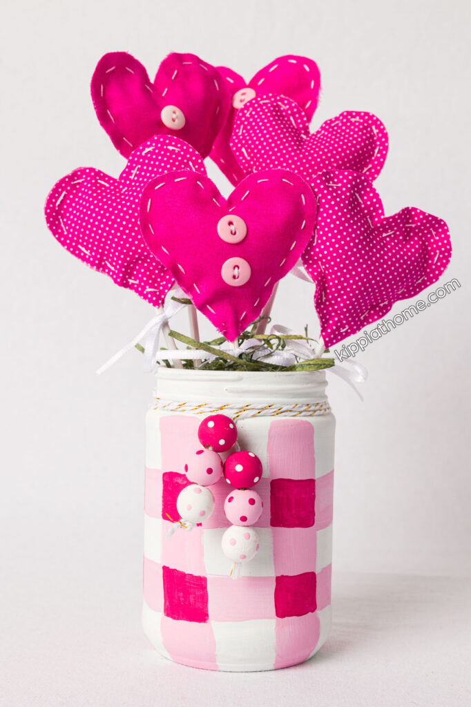 handmade pink fabric hearts in a buffalo check painted jar sitting on a table