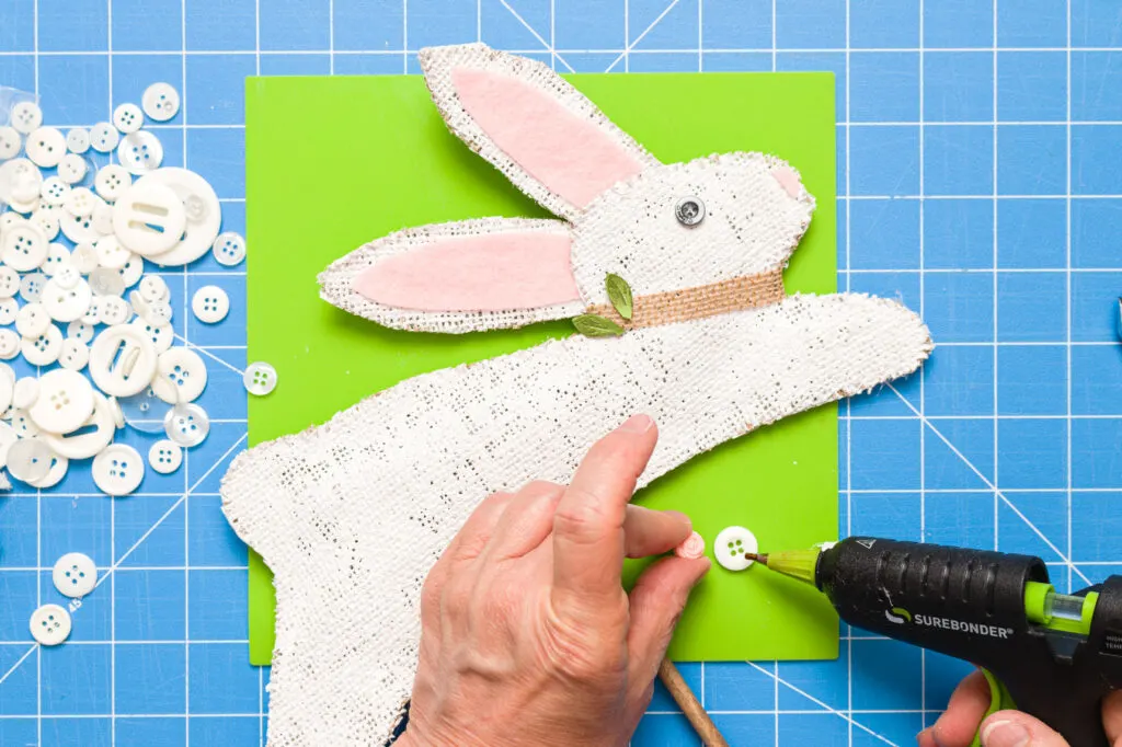 Decorating the bunny with a burlap collar, button flower and green leaves on a silicone mat 