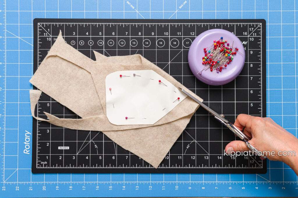 Cutting out the body pattern out of tan felt fabric on a craft mat