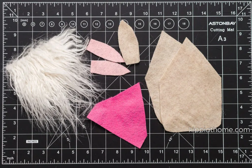 Felt and fur pieces cut out and sitting a craft mat