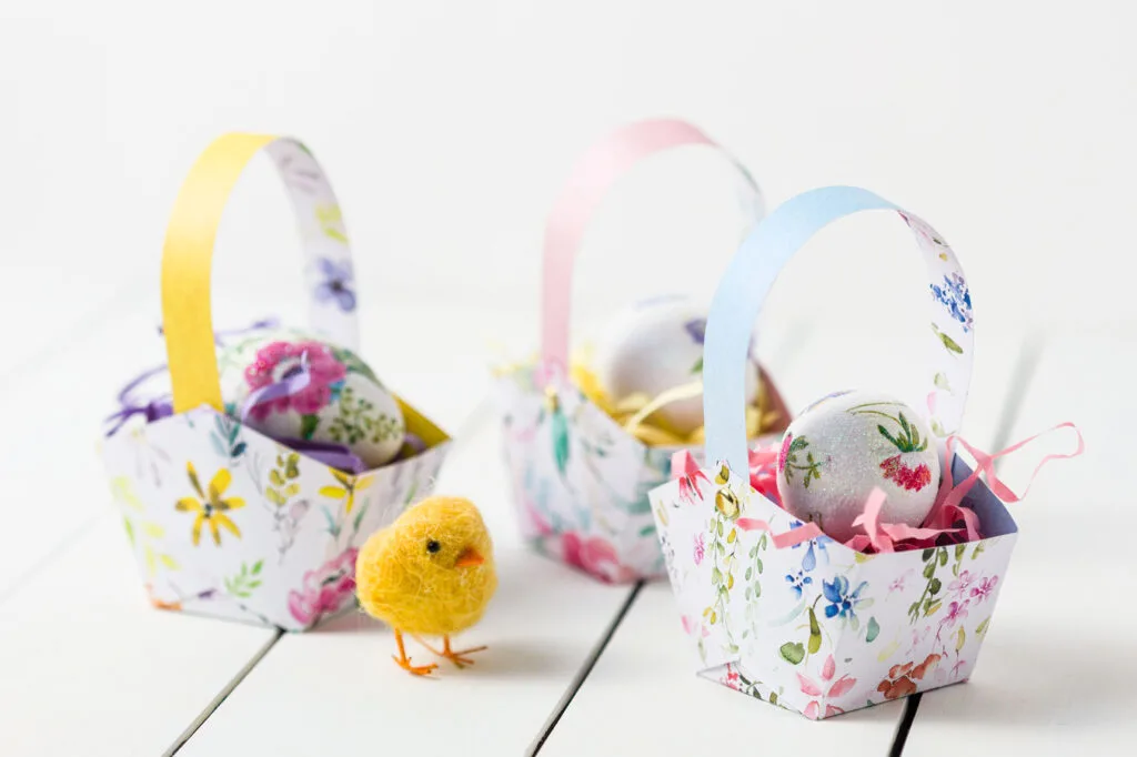 three Easter paper Baskets with eggs and a chick on a wood table
