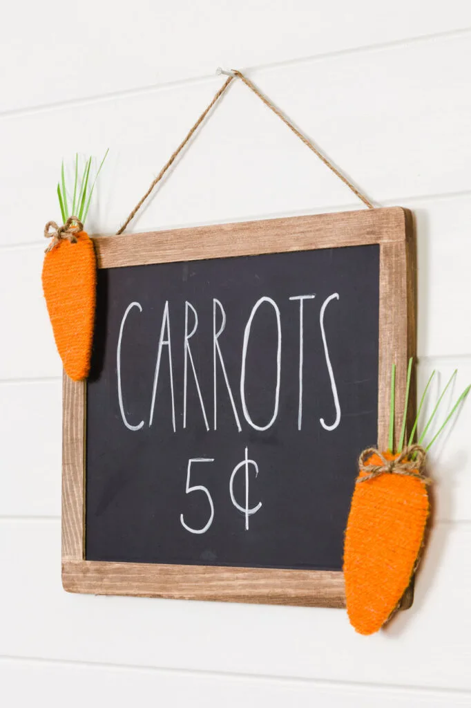 Chalkboard sign with handmade yarn carrots hanging on a white wall