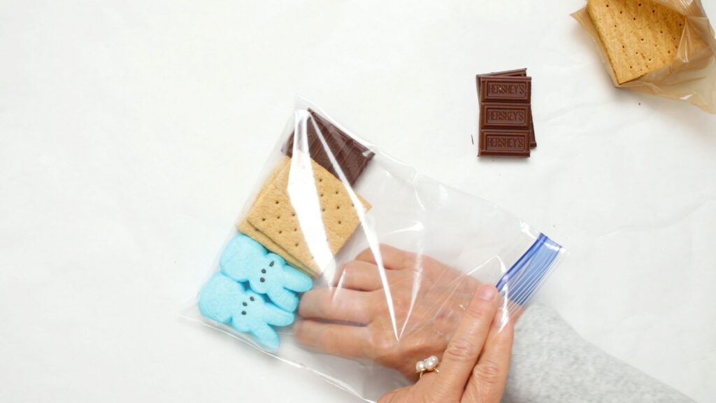 Plastic bag filled with chocolate candy bar, graham crackers, and two marshmallow candies